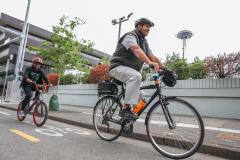 Black man and child pedal down a protected bike lane in a downtown area